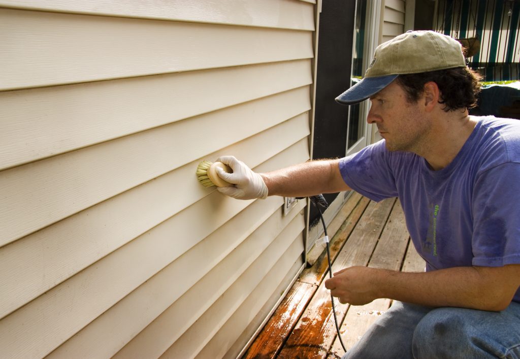 man washing house's siding by hand with a brush